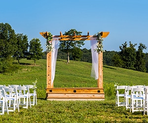 Decorated wedding trellis and white chairs on grassy hill at Matilda's Event Barn