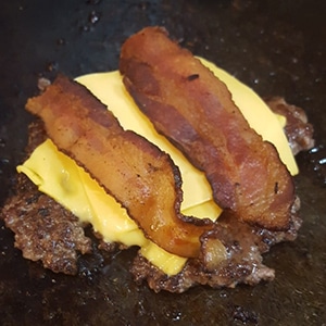 Hamburger with cheese and bacons on a flat grill