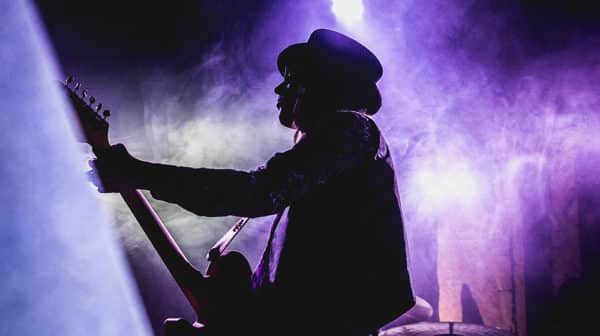 Shadow of a man in hat playing guitar with purple lights in background