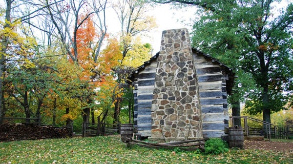 Side view of the cabin at the Living Historical Farm shows the fireplace with colorful fall trees in the background