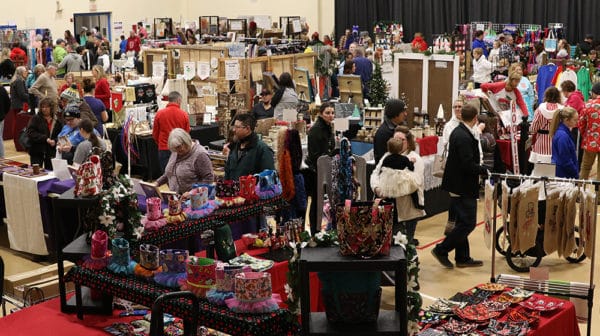 Crowds of shopper mill around vendor tables at an arts and crafts show in a school gymnasium