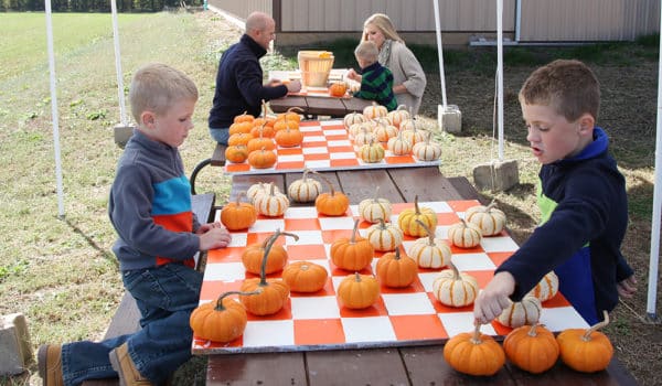 Two young boys playing checkers with mini pumpkins, with parents and younger boy playing checkers in the background