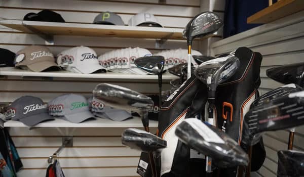 Golf bag and clubs set in front of three shelves holding a display of various golf-branded hats