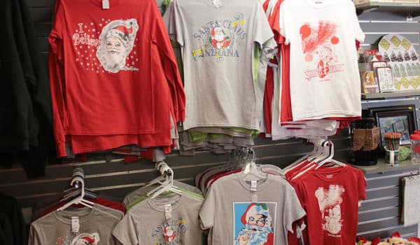 A selection of Santa Claus-themed t-shirts hang in two rows on a wall
