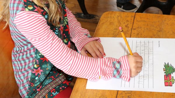 Close up of little girl from neck down wearing a Christmas outfit and writing a letter at an old-fashioned desk