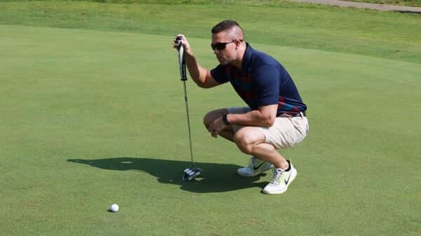 Golfer holding a golf club squats and studies the ball in front of him