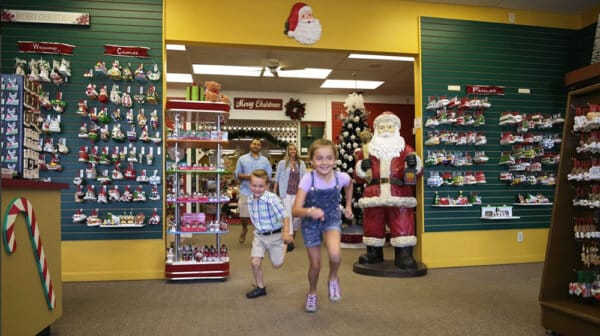A boy and girl run forward through the ornament shop at the Santa Claus Christmas Store as their parents follow in the background