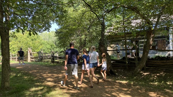 Family of four walks past Living Historical Farm cabin at Lincoln Boyhood National Memorial as a cameraman films them for a destination video
