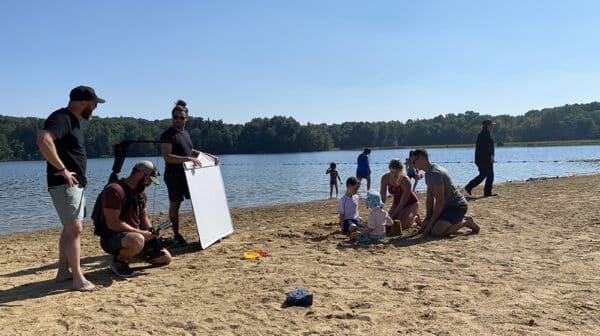 Parents and kids play on beach at Lake Lincoln while camera crew films them for a destination video