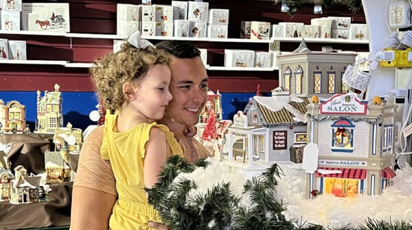 Dad holds daughter and looks at collectible villages at Santa Claus Christmas Store during destination video shoot