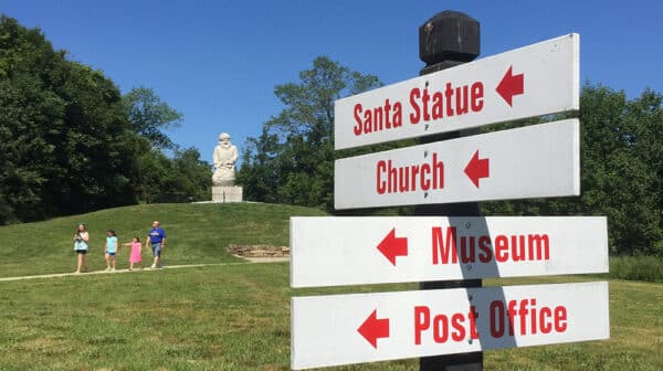 Directional signs marking locations at Santa Claus Museum & Village shown in foreground with historic Santa statue in background