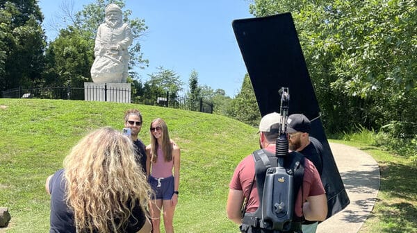 Young man and woman take a selfie in front of the historic Santa statue at the Santa Claus Museum & Village as a film crew shoots them for a destination video