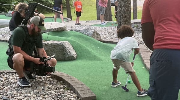 Young boy playing mini golf at Sun Outdoors Lake Rudolph is filmed by cameraman for destination video