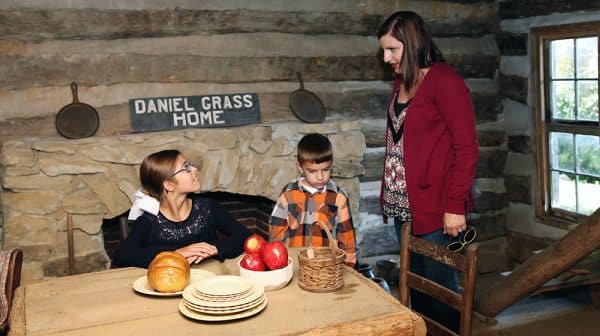 Mom, son, and daughter explore the inside of a cabin at Lincoln Pioneer Village & Museum