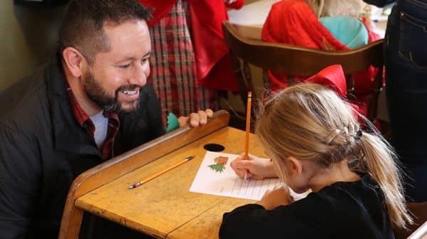 Young girl writes a letter to Santa at the Santa Claus Museum & Village while her father watches
