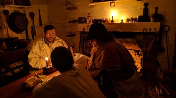 Three men sit inside the candlelight cabin at the Living Historical Farm at Lincoln Boyhood National Memorial