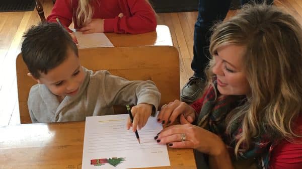 Woman helps little boy sitting at old-fashioned school desk write a letter to Santa at the Santa Claus Museum & Village