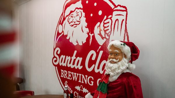Santa Claus Brewing Co. logo is featured on a wall in the taproom next to a table and Santa statue